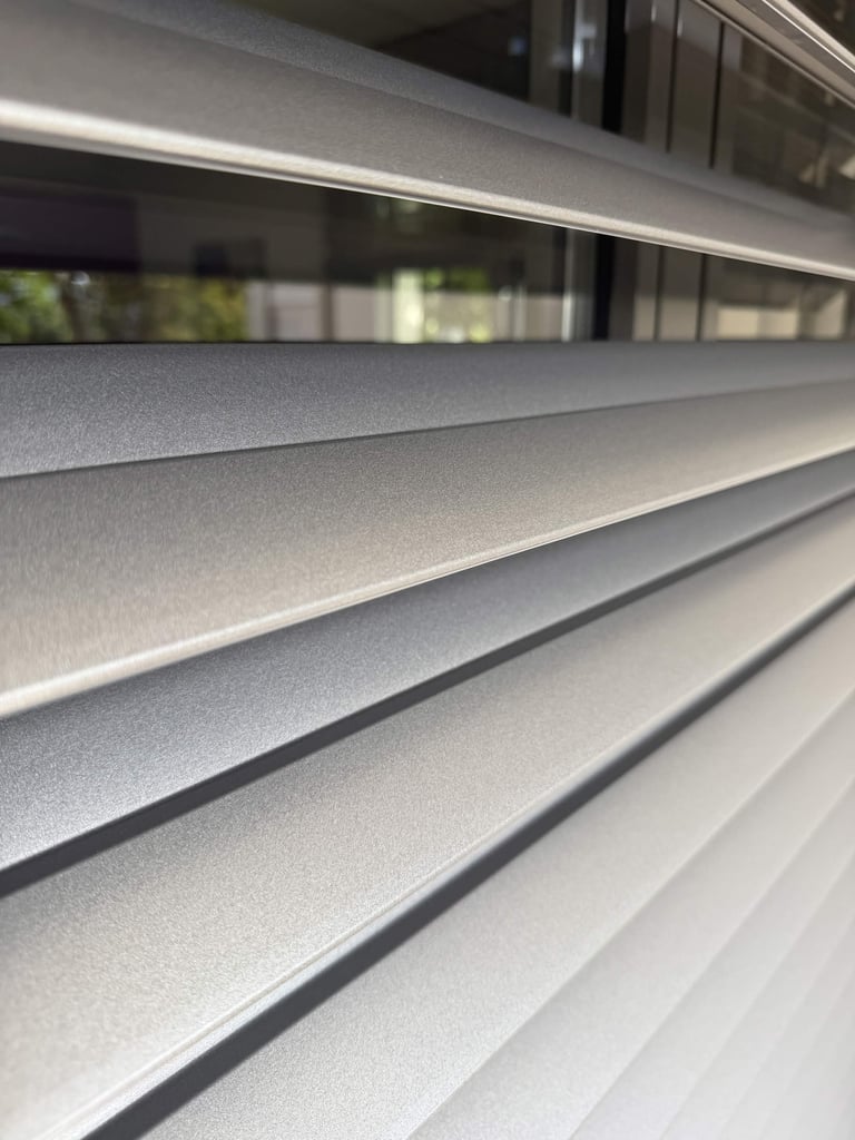Close-up of horizontal metallic roller blinds with window reflection in background
